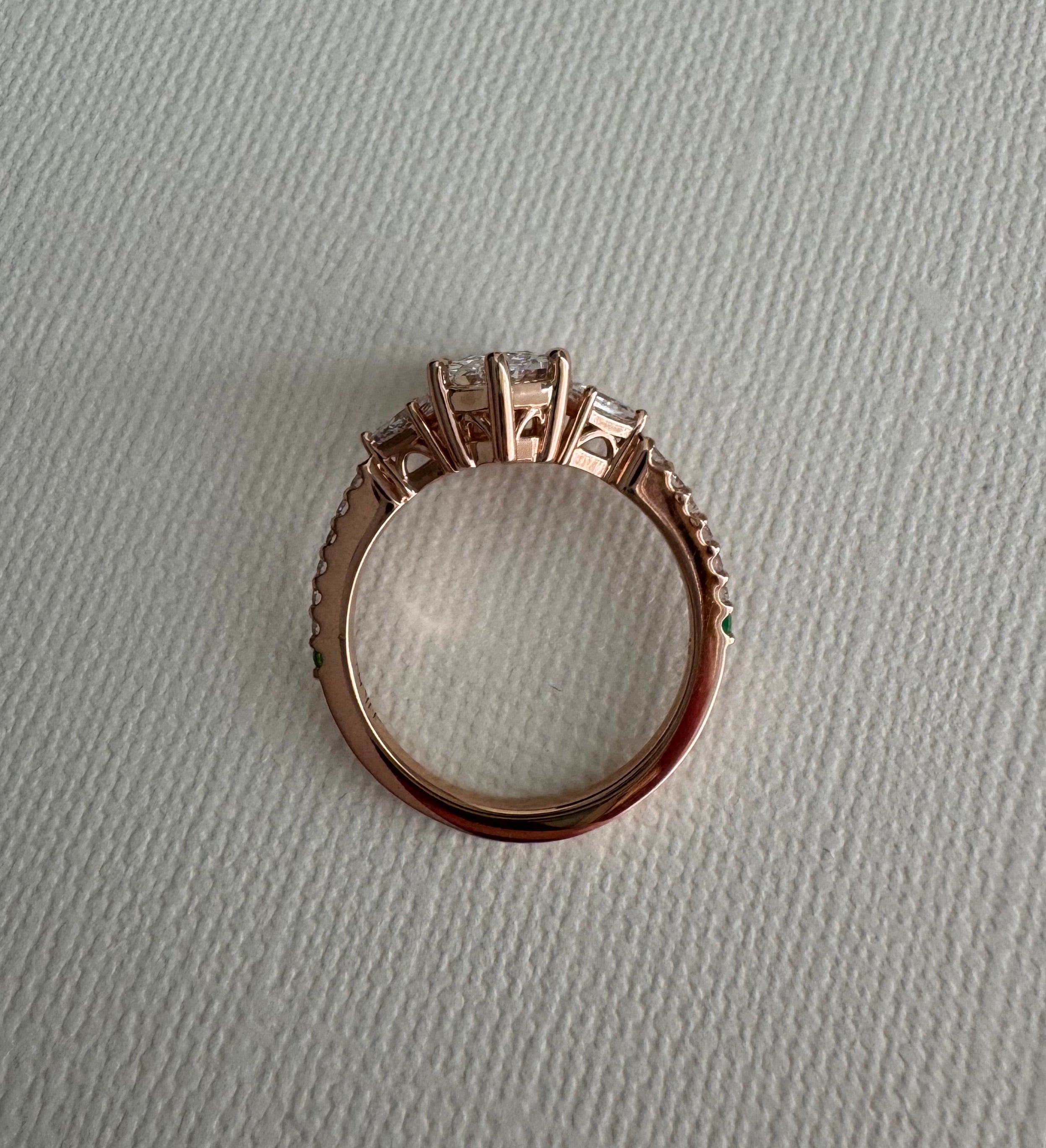 Custom 14k rose gold lab grown diamond engagement ring. Center= 1.69 ct lab grown elongated hexagon. Accents are 2 lab grown kite diamonds (0.29 cttw), 12 lab grown round diamonds (approx 0.18 cttw), 1 round emerald, 1 round tsavorite garnet. Size 8.5.