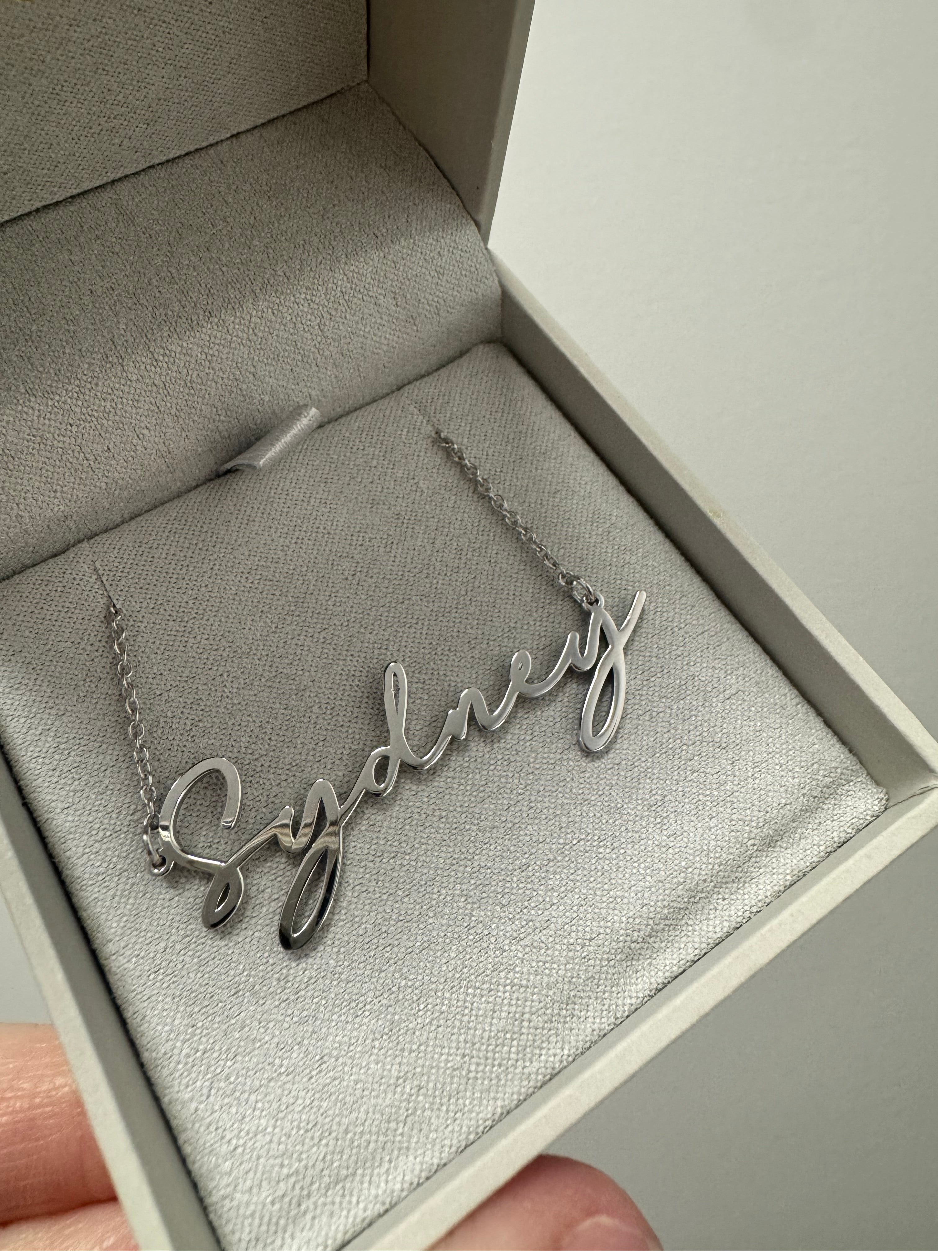 Rhodium-plated sterling silver name plate necklace in Bathinda font with the name "Sydney". 18", 1.25mm rh. plated sterling silver cable chain with lobster clasp.