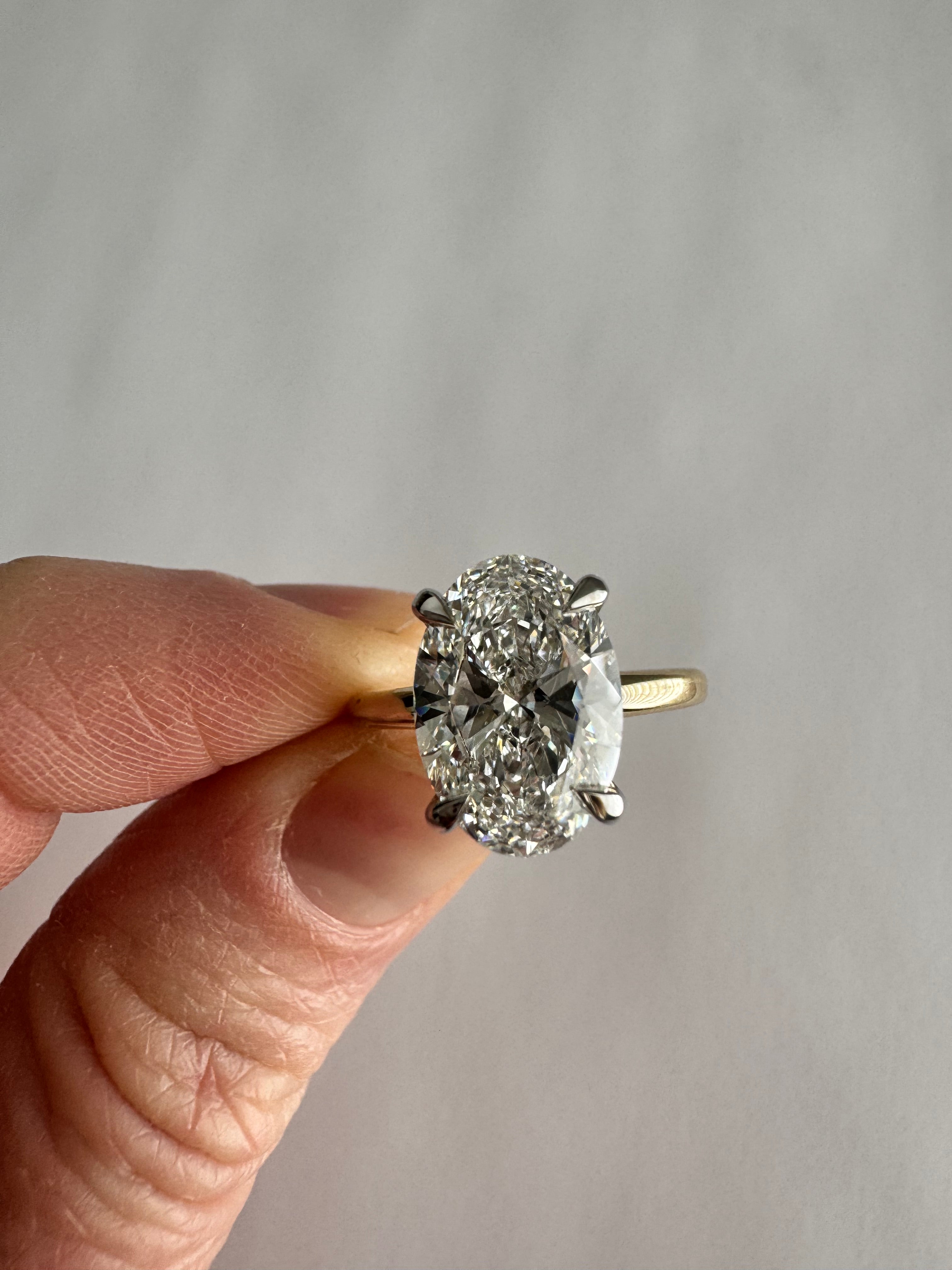 Custom, 14k yellow gold engagement ring with 14k white gold hidden halo 4 prong head. 3.03 ct lab grown oval diamond center (D, VS1). Size 5.