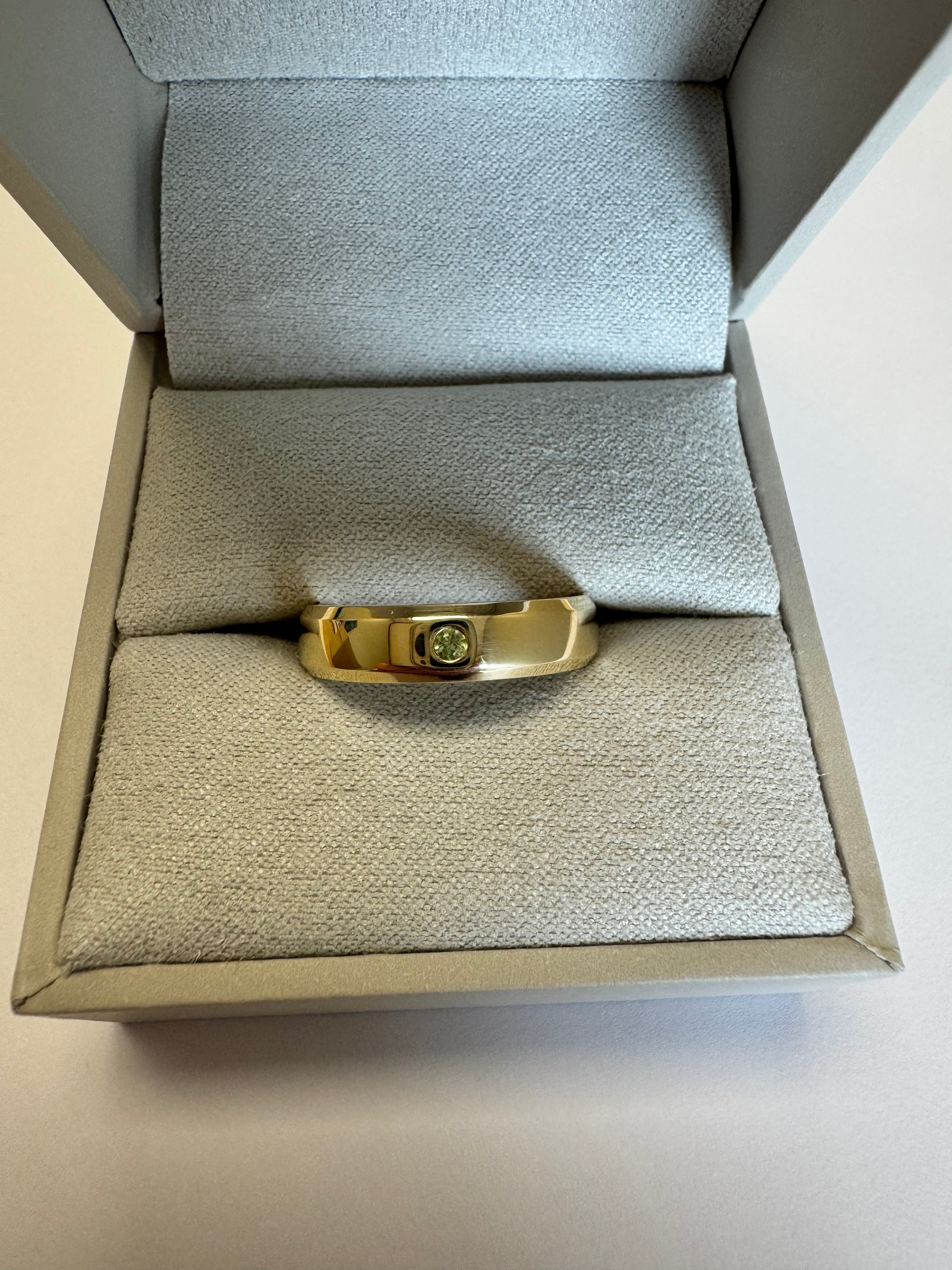10k yellow gold 5mm wide, beveled edge half round wedding band with a 2mm genuine peridot (AA quality) flush set. Engraved on the inside in Bookman font: "AW+JS   05.23" There is a special character between the JS and the 05 (upside down V) Size 8.