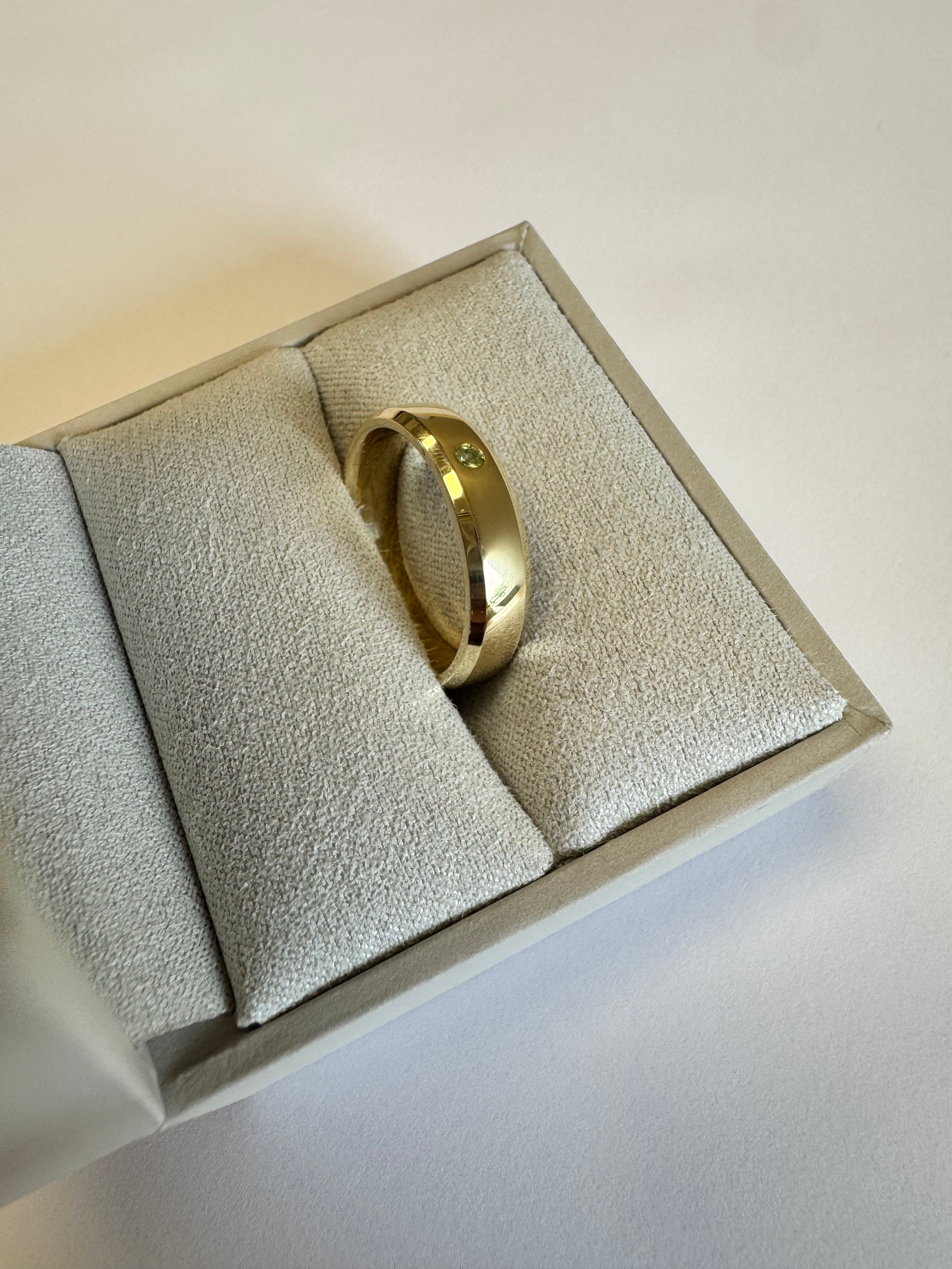 10k yellow gold 5mm wide, beveled edge half round wedding band with a 2mm genuine peridot (AA quality) flush set. Engraved on the inside in Bookman font: "AW+JS   05.23" There is a special character between the JS and the 05 (upside down V) Size 8.